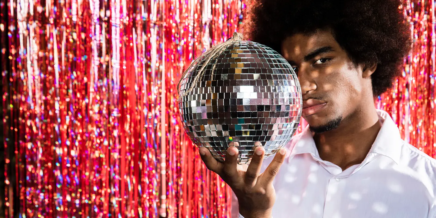 Man holding a disco ball in front of red tinsel backdrop