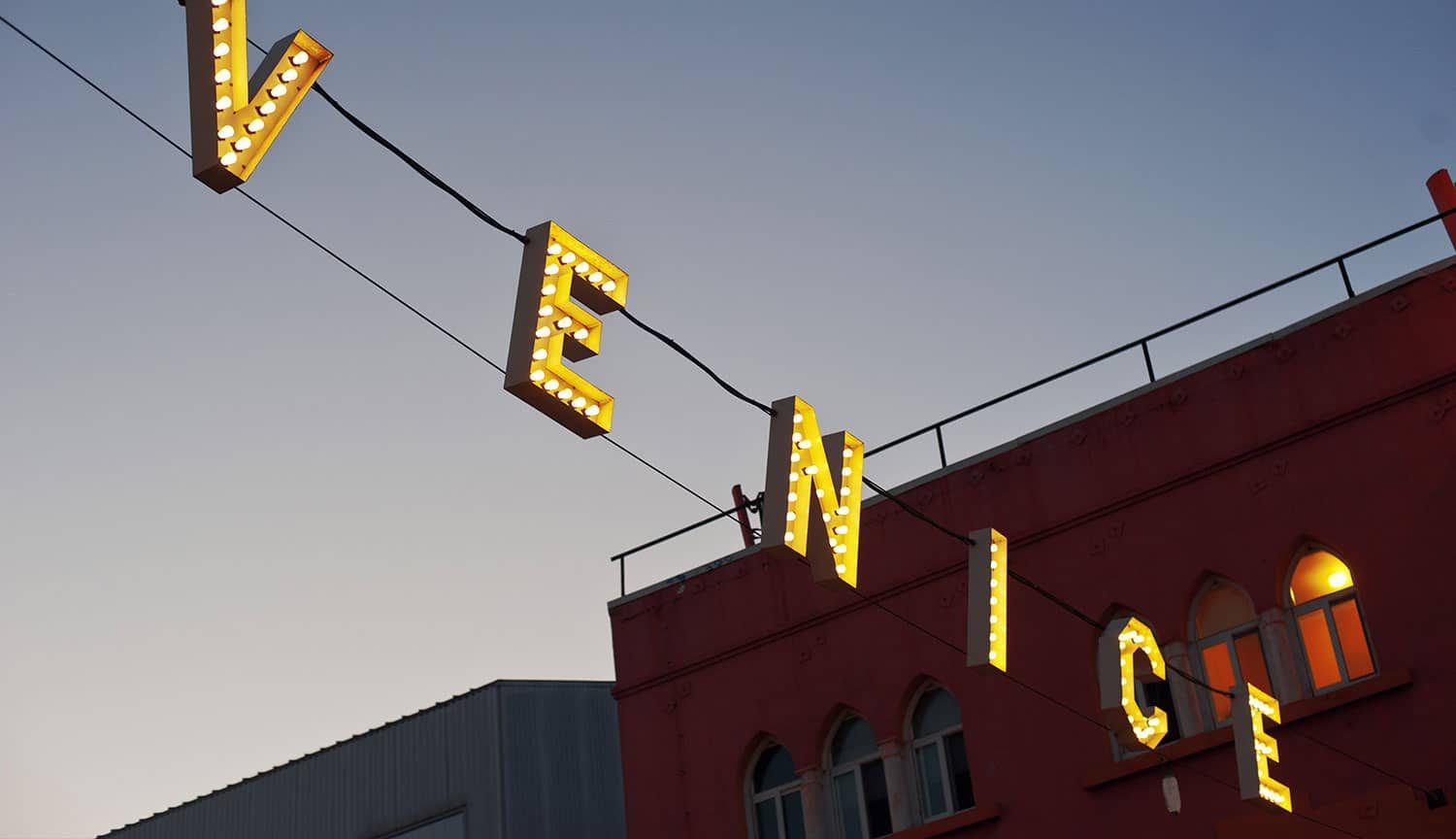 Venice sign glowing above a red brick building at dusk